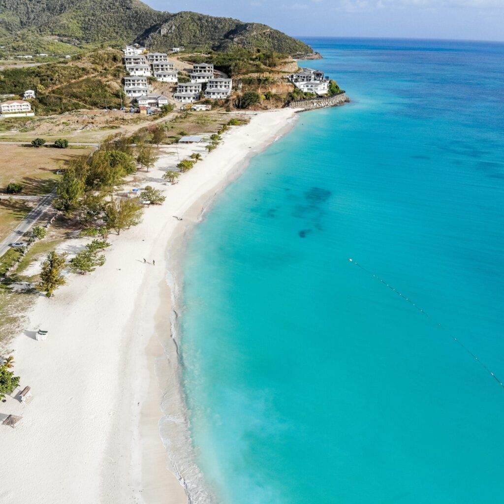 Aerial view of a white-sand beach with turquoise water and hillside villas in Antigua