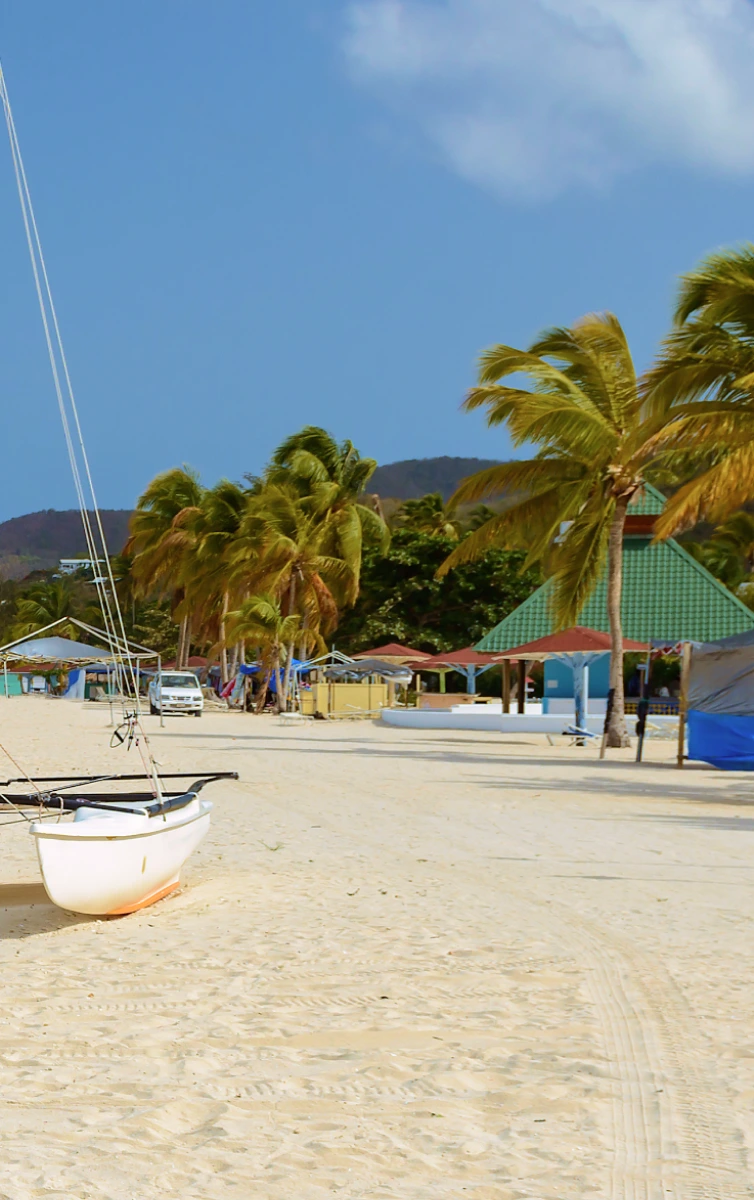 Sandy beach with a beached sailboat, palm trees and a beach bar