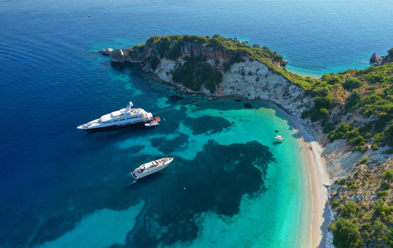 Luxury yachts anchored off a rocky coastline in turquoise water