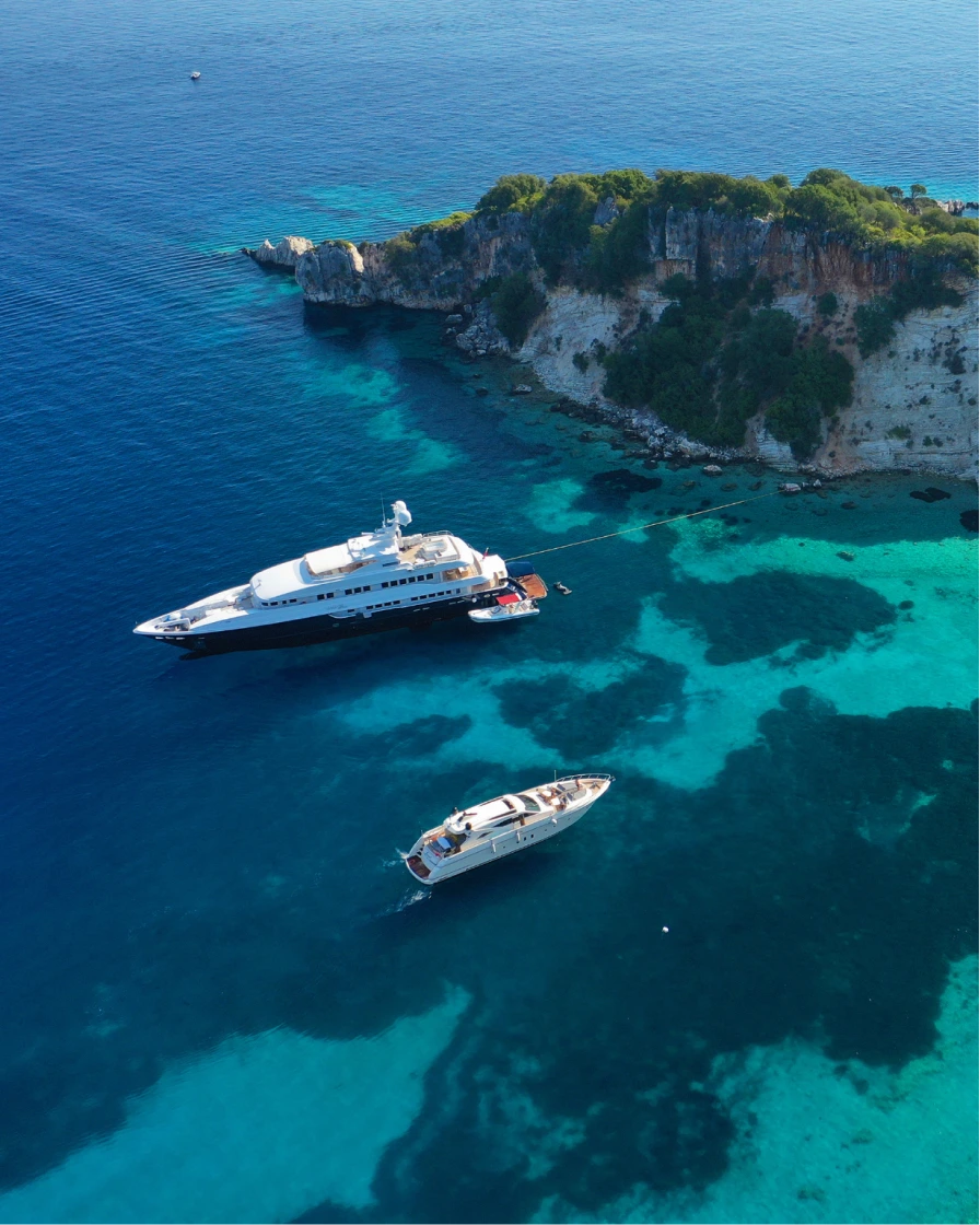 Luxury yachts anchored off a rocky coastline in turquoise water