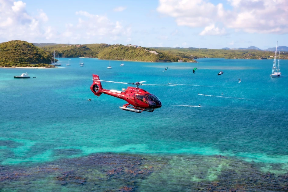 Red helicopter flying over a turquoise bay in Antigua